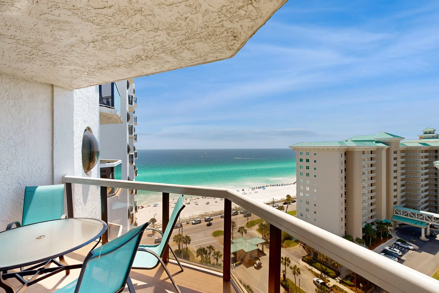 A balcony overlooks the ocean, beach, and nearby buildings.