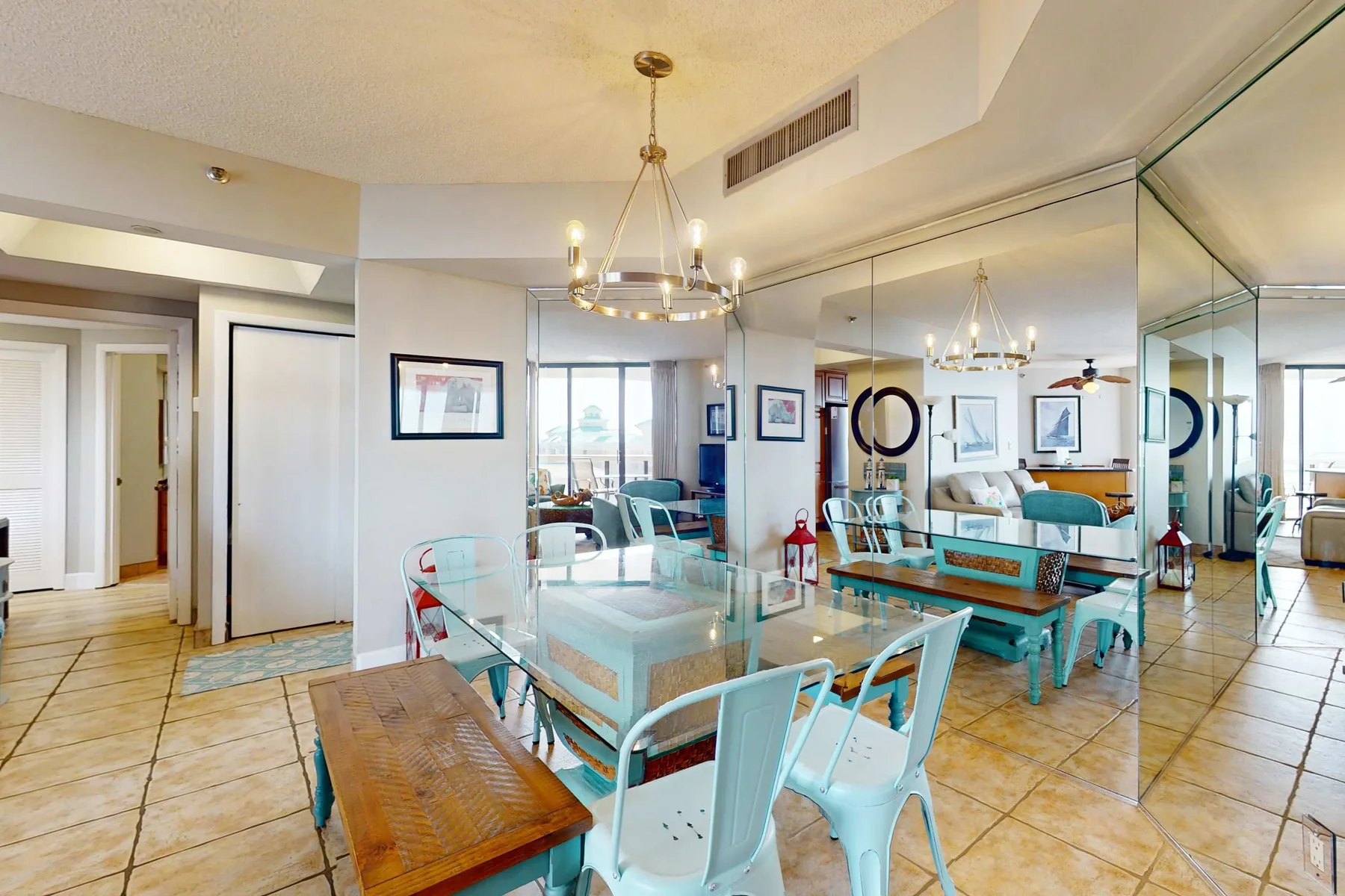 A dining area with a glass table and turquoise seating, reflected in a mirrored wall.
