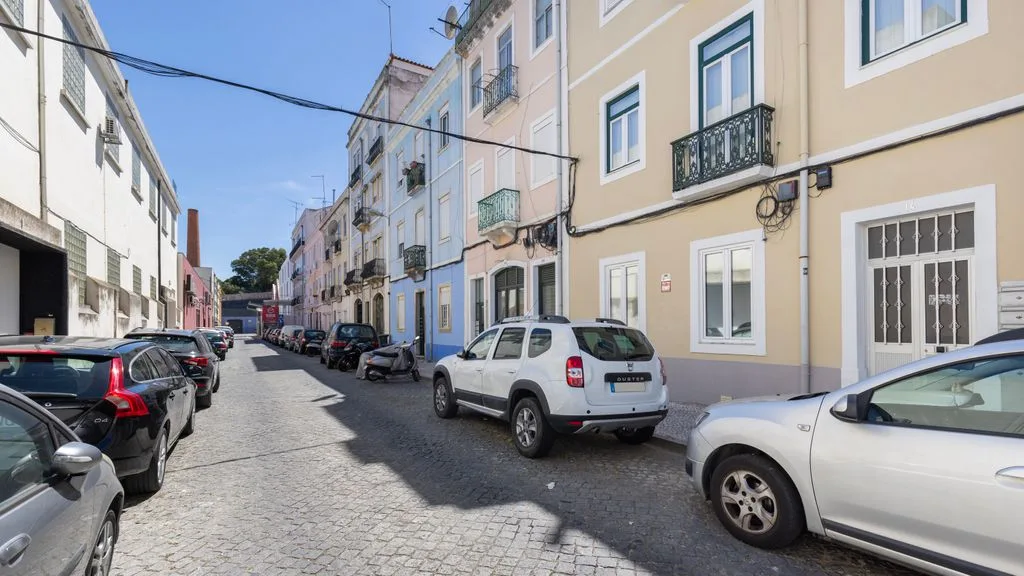 Una calle estrecha adoquinada, con coches aparcados y edificios de colores.