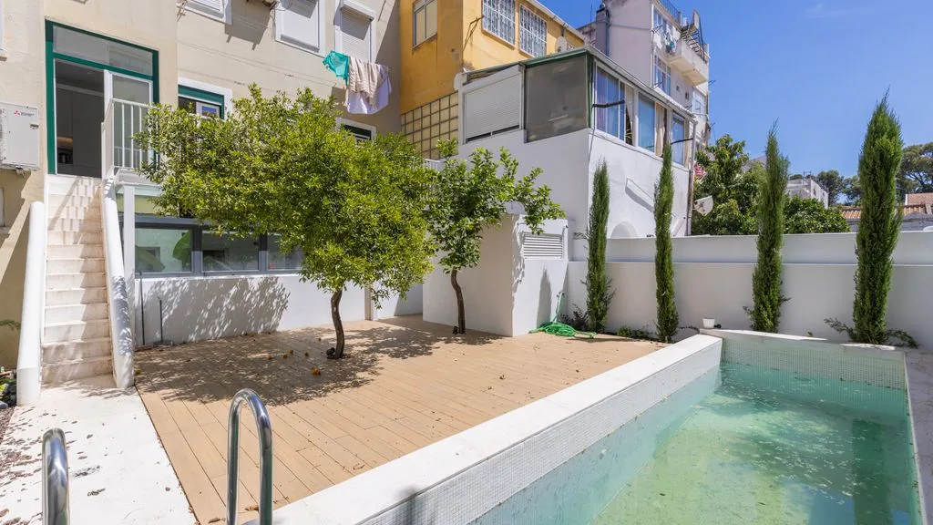 Una pequeña piscina de patio está junto a una terraza pavimentada y árboles frondosos.