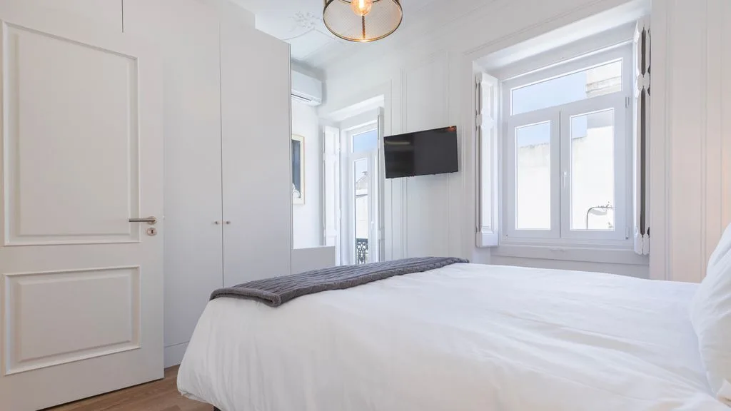 Un dormitorio luminoso con una cama bien hecha y un televisor en la pared.