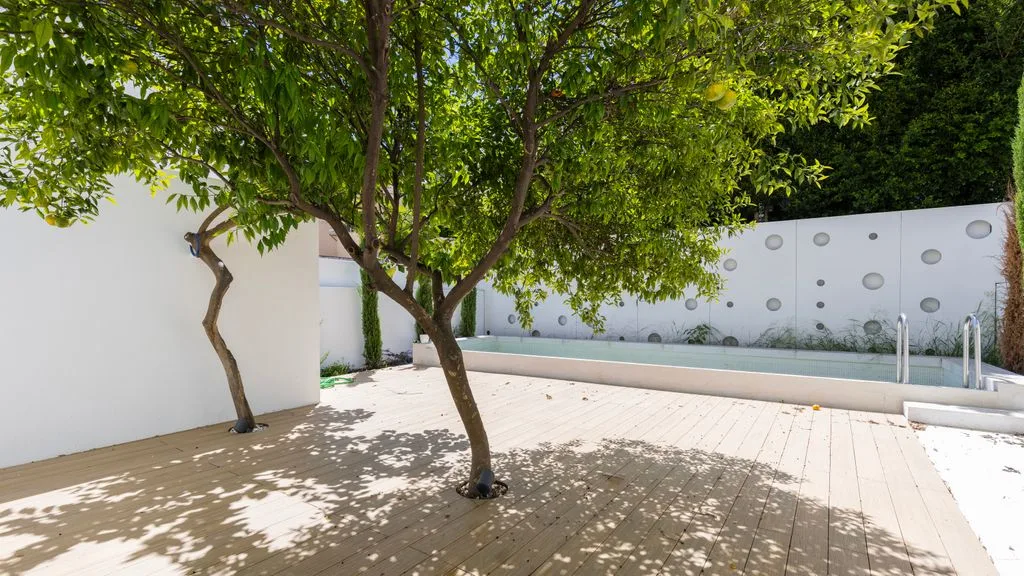 Un árbol da sombra a un patio pavimentado junto a la piscina.