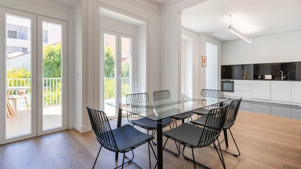 Un comedor luminoso con una mesa de vidrio y puertas que dan a un balcón.