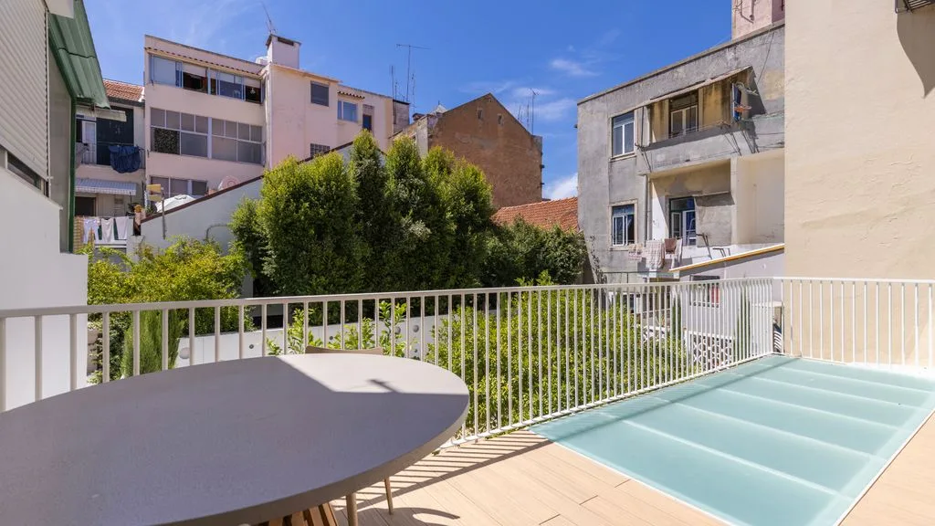 Una terraza soleada da a una piscina cubierta de cristal y a edificios cercanos.
