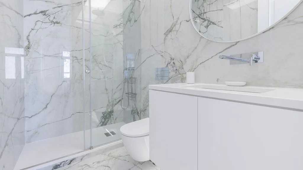 Un baño luminoso con ducha de vidrio y un tocador blanco.