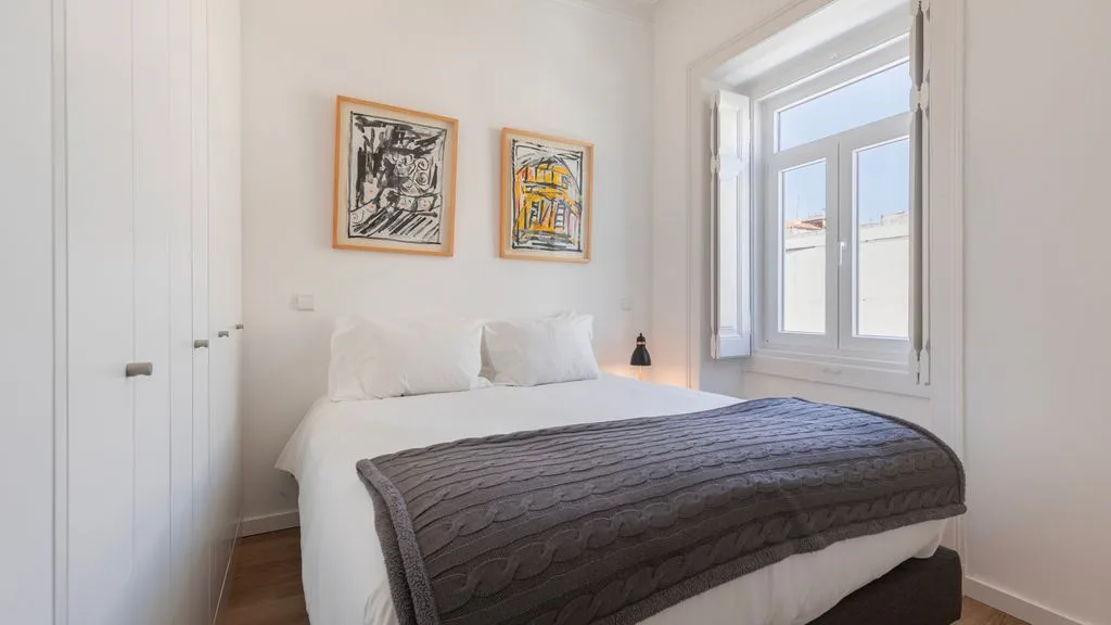 Un dormitorio luminoso con una cama tendida y cuadros enmarcados.