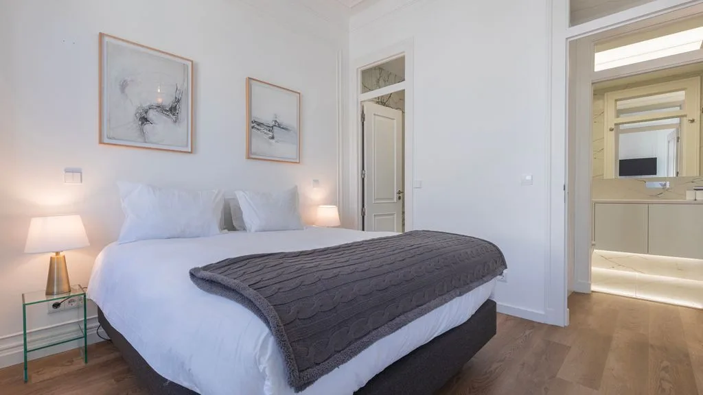 Un dormitorio luminoso con una cama hecha y cuadros enmarcados en la pared.