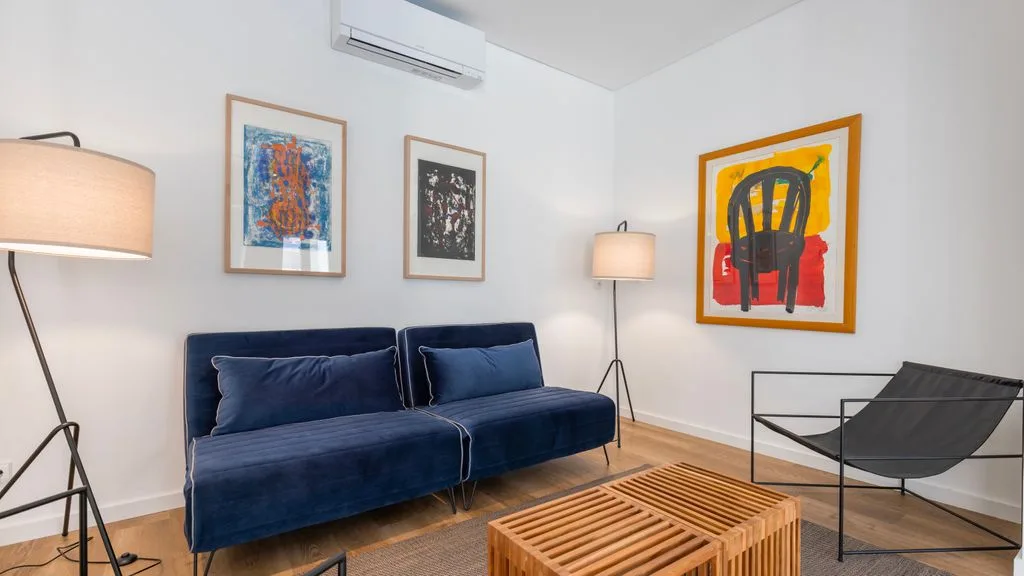 Una sala de estar con un sofá azul, cuadros enmarcados y una mesa de centro con listones.