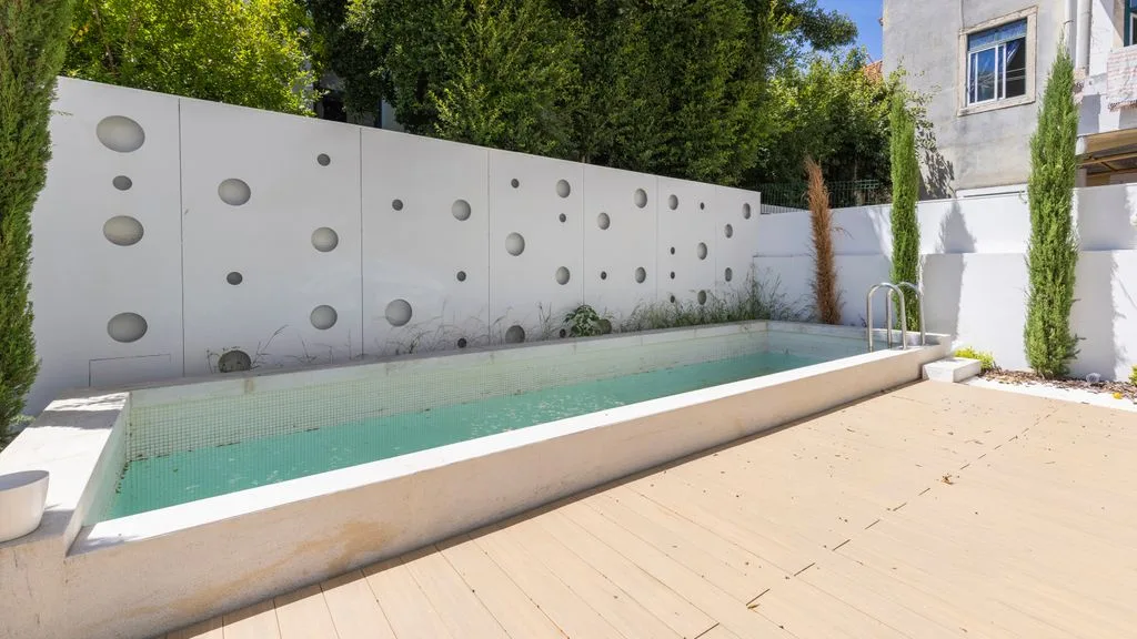 Una pequeña piscina exterior está junto a una pared decorada y un patio soleado.