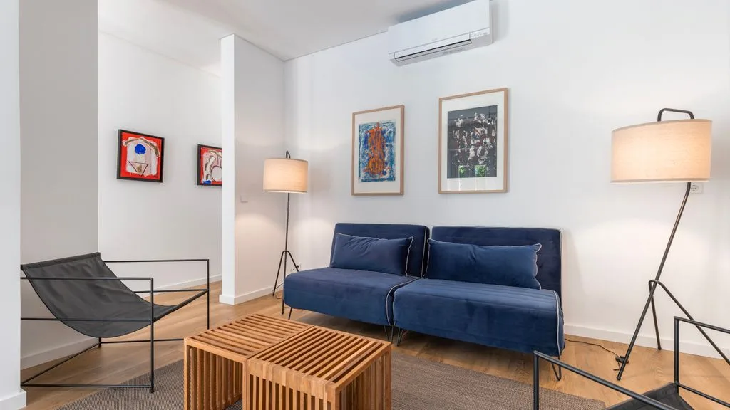 Una sala de estar luminosa con asientos azules, mesas de madera y cuadros.