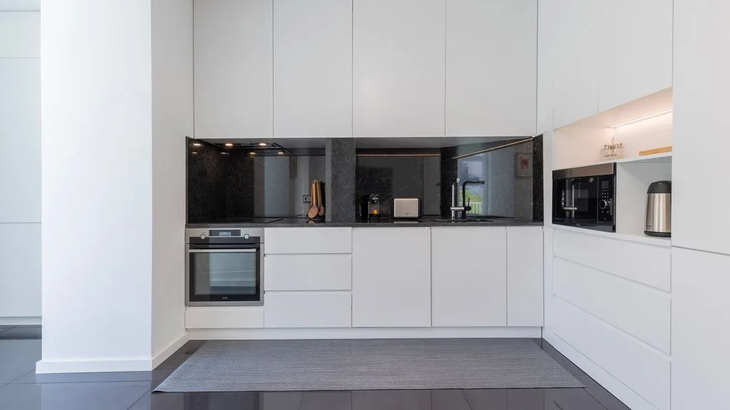 Una cocina moderna blanca con electrodomésticos integrados y un salpicadero oscuro.