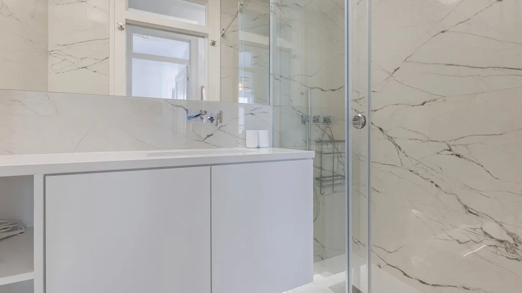Un baño luminoso con una ducha de cristal y paredes claras con vetas.