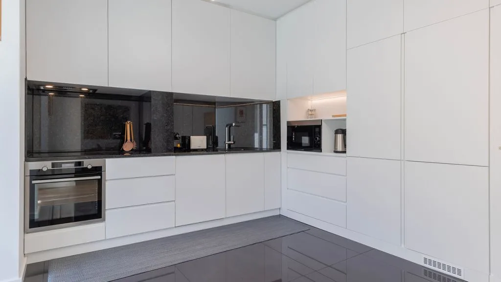 Una cocina moderna con gabinetes blancos, un salpicadero oscuro y electrodomésticos integrados.