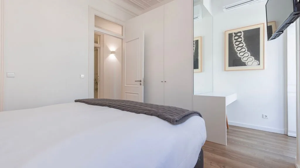 Un dormitorio luminoso con ropa de cama blanca y una obra enmarcada en la pared.