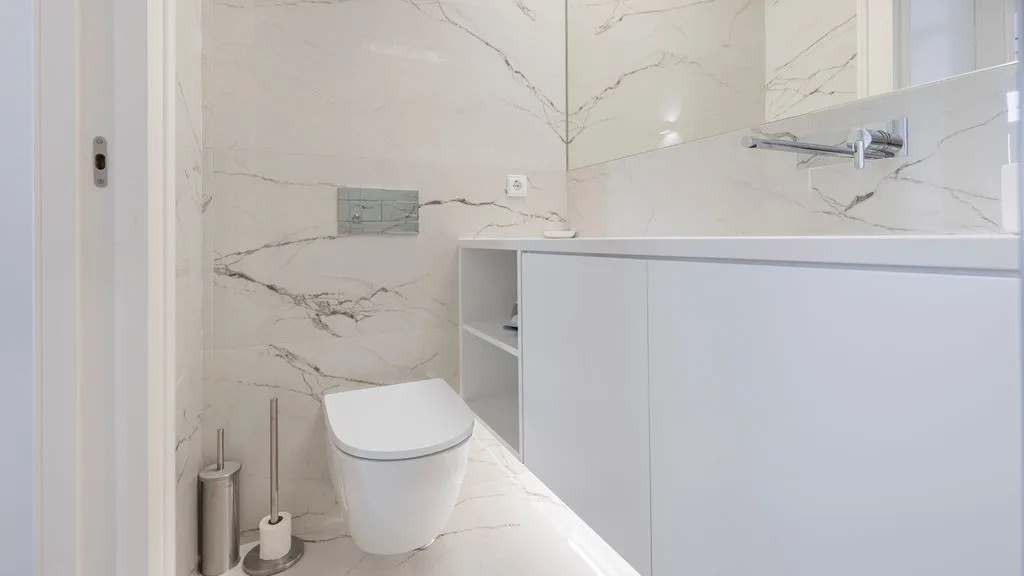 Un baño con inodoro suspendido y mueble de lavabo blanco.
