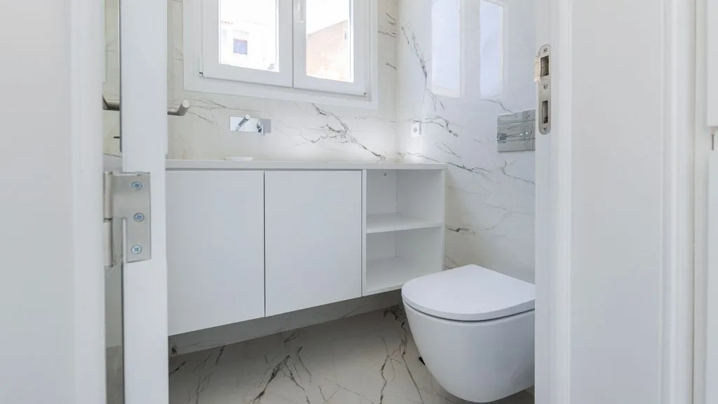 Un baño luminoso con un inodoro suspendido y un mueble blanco.