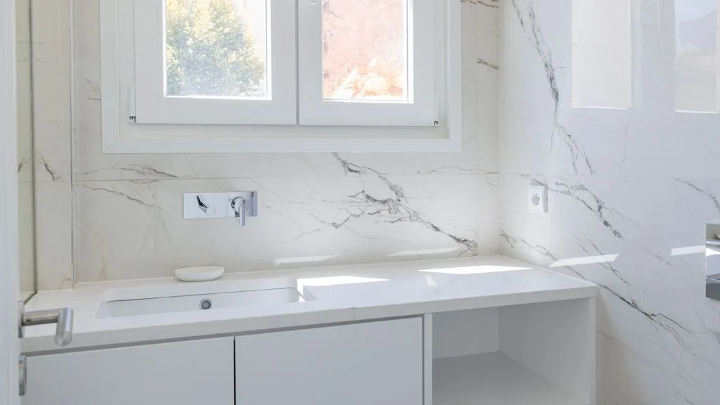 Un baño luminoso con un largo lavabo bajo una ventana.