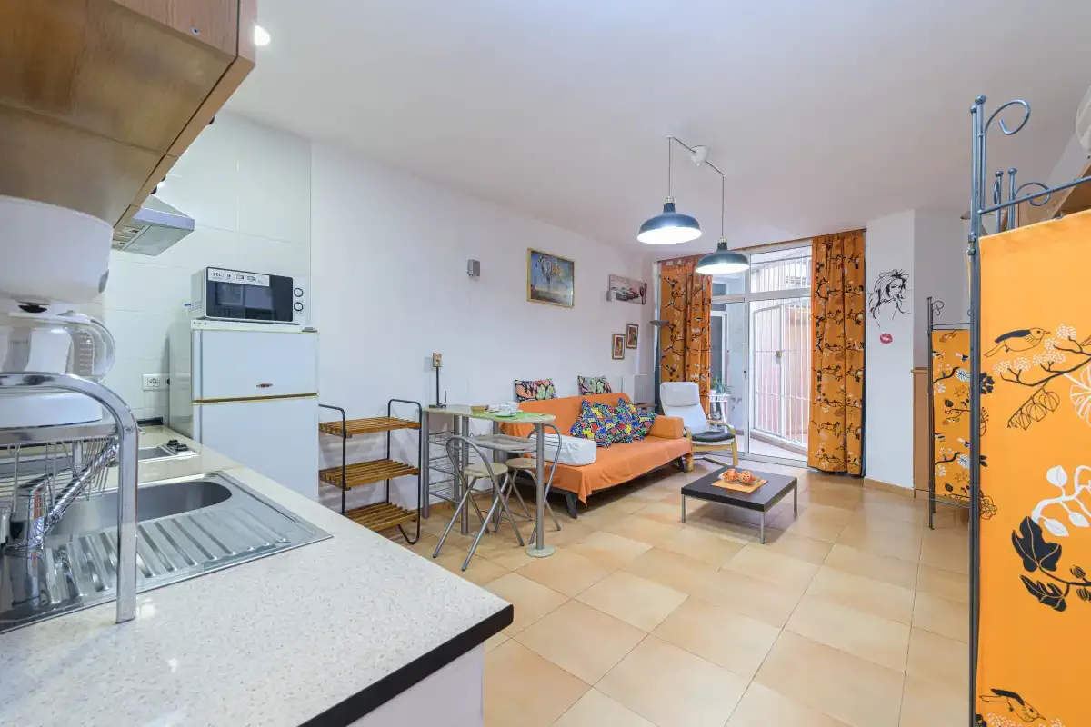 A studio living area with a small dining table and orange curtains.