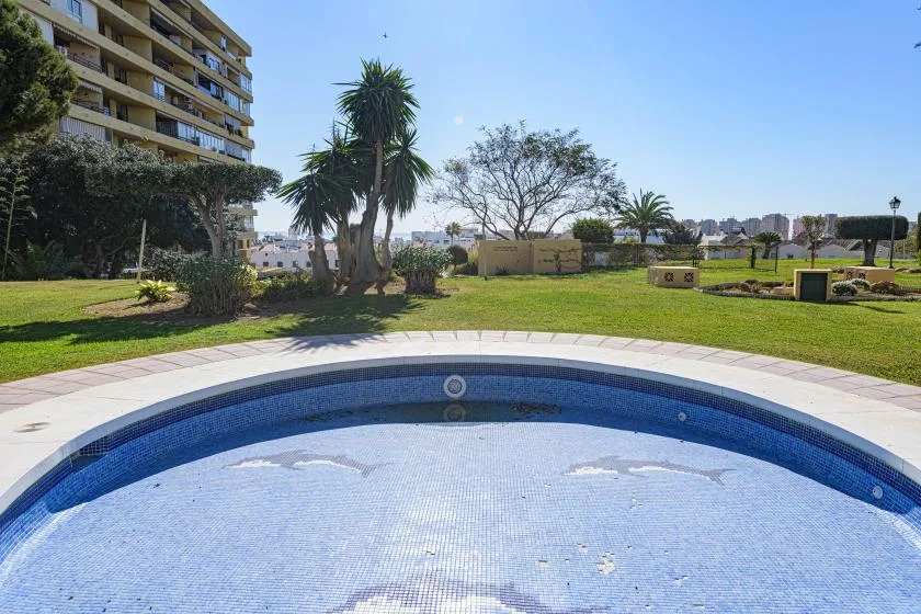 A swimming pool beside a grassy garden and apartment building.