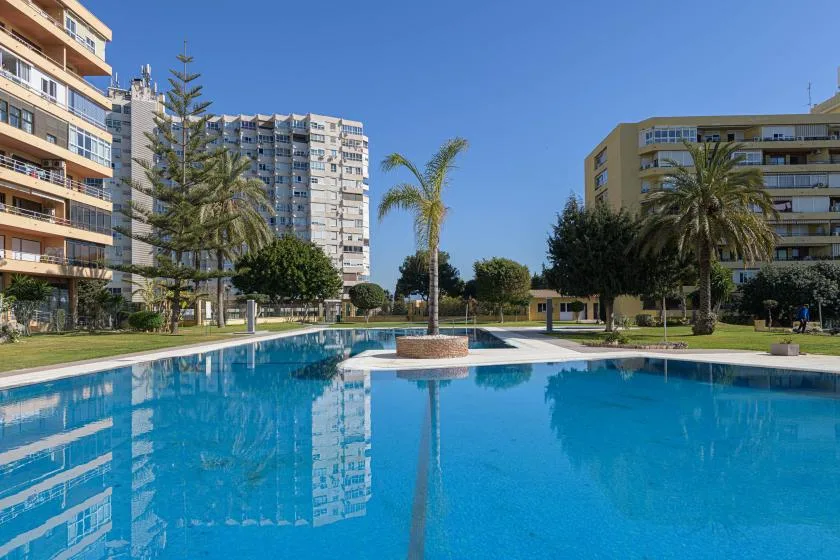 Outdoor swimming pool surrounded by apartment buildings, palm trees, and landscaped grounds.