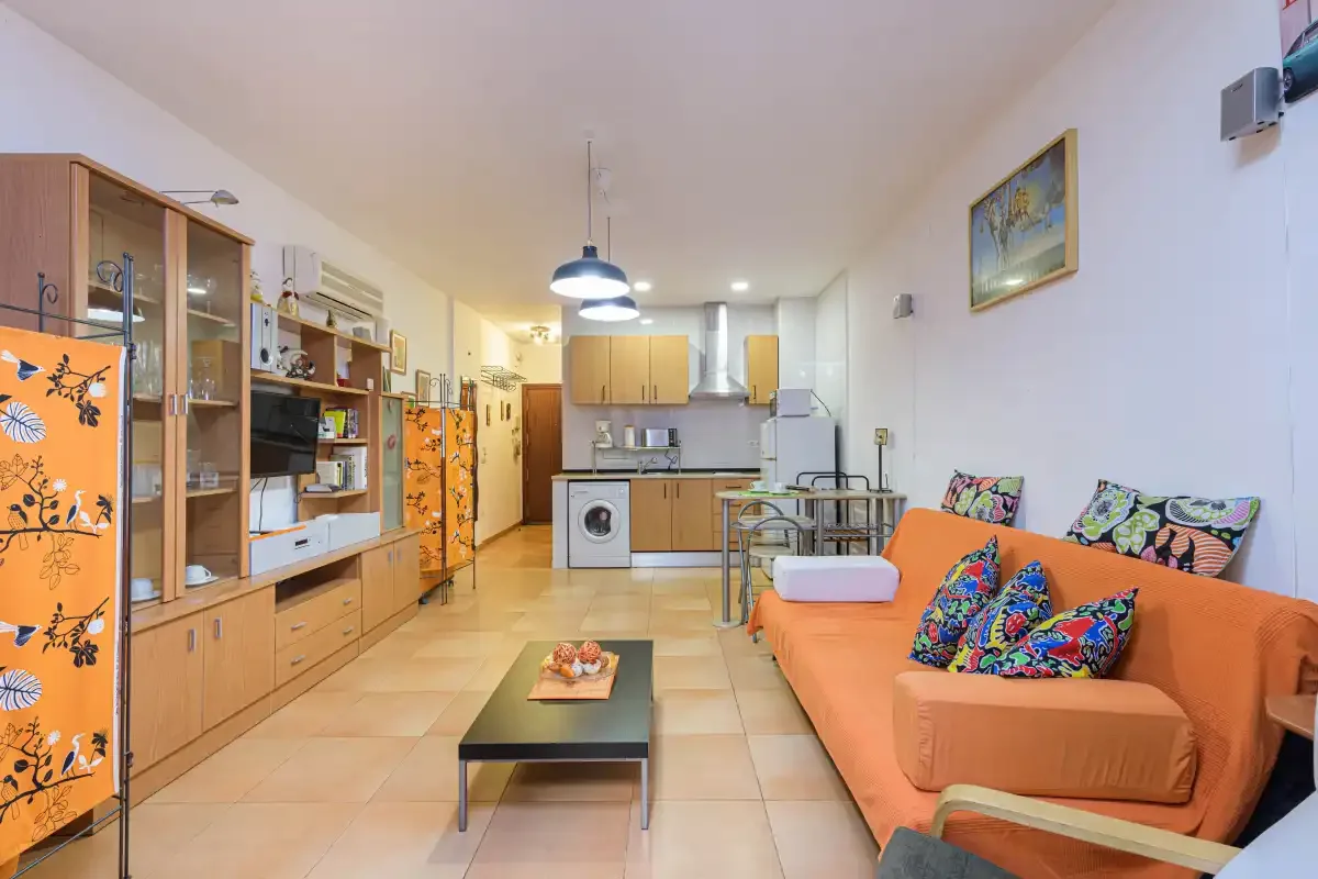 A compact living area opens onto a kitchen, with orange seating and a coffee table.