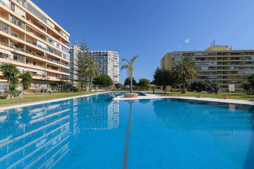 An outdoor swimming pool sits among landscaped grounds and multistory buildings.