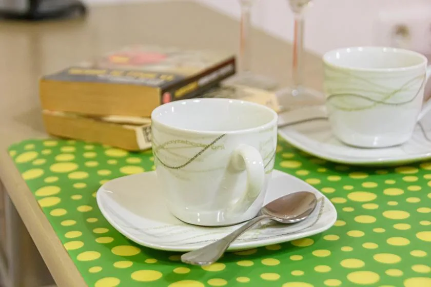 Two cups and saucers sit on a green polka-dot tablecloth beside a book.