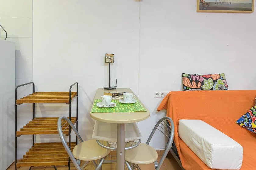A small dining area with a table and chairs beside an orange-covered bed.