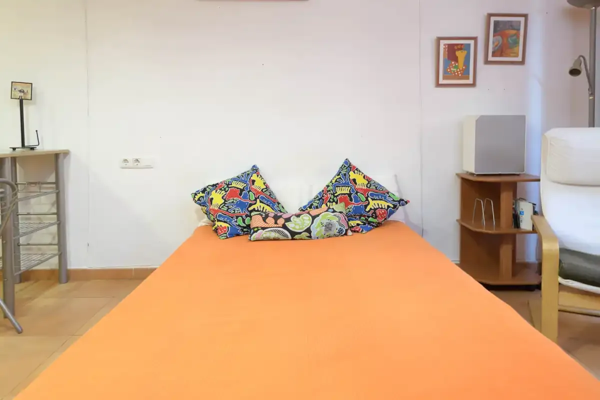 A bedroom with an orange bedspread and colorful patterned pillows.