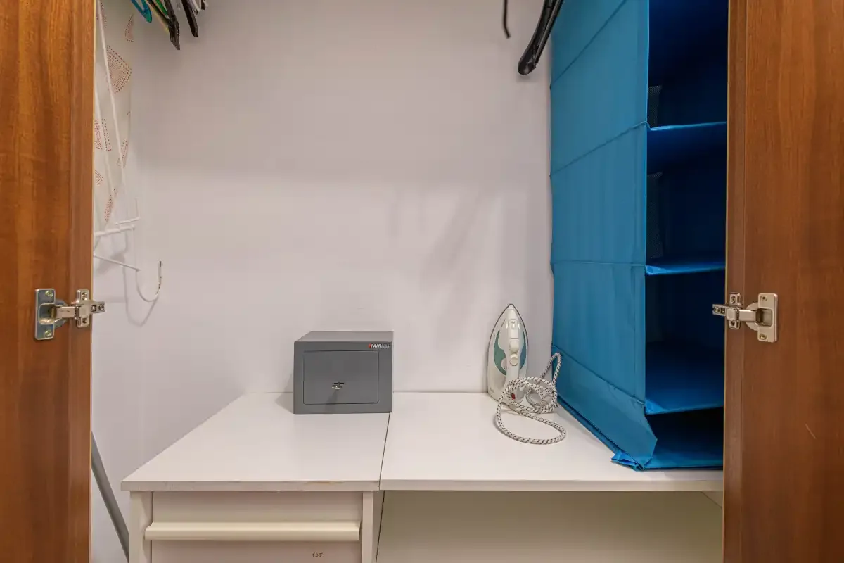 A compact desk area with a small safe and an iron beside blue shelving.