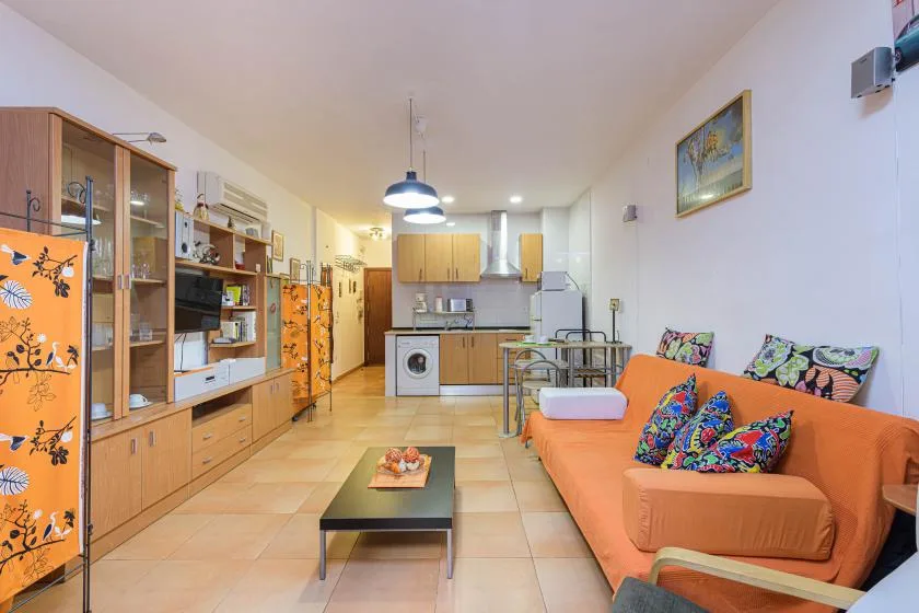 A living room with an orange sofa and an open kitchen in the background.