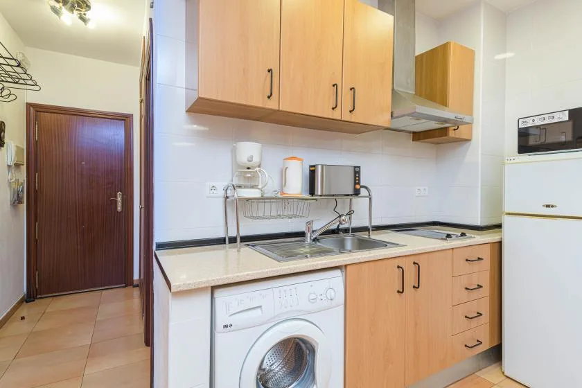 A compact kitchen with wooden cabinets, a sink, and a washing machine.