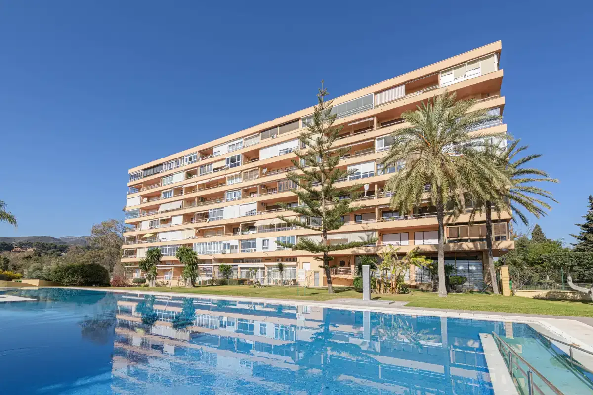 A multi-story building stands beside a swimming pool under a clear blue sky.