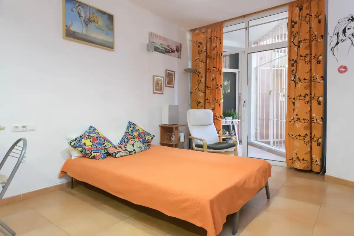 A bedroom with an orange-covered bed beside a glass door.