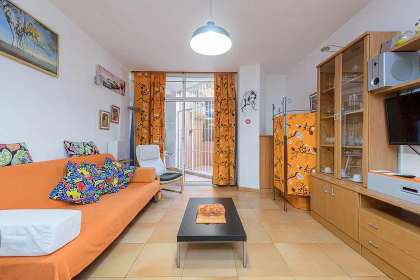 A living room with orange seating, a coffee table, and glass doors to a balcony.
