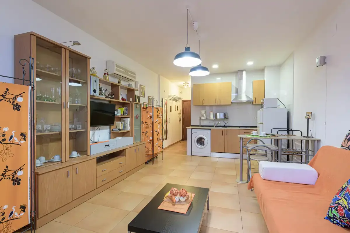 A furnished studio interior with a kitchenette, dining table, and seating area.