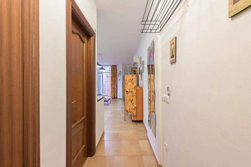 A narrow hallway has tiled flooring, wooden doors, and colorful wall decorations.