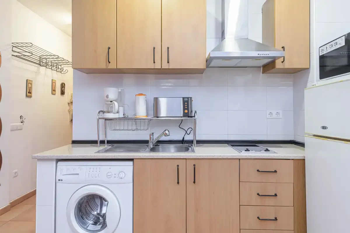 A compact kitchen with wooden cabinets, a sink, and a washing machine.