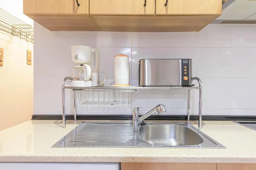 A kitchen counter with a sink, dish rack, and small appliances beneath wooden cabinets.