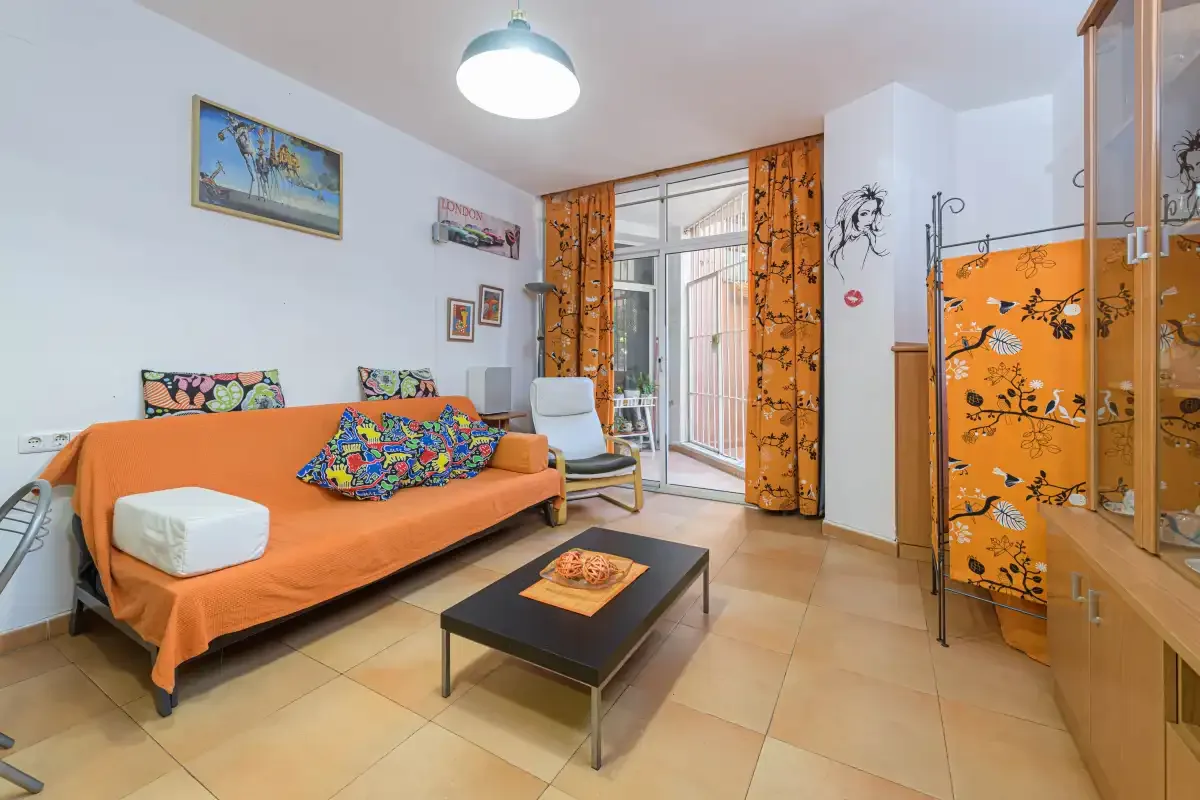 A living room with orange seating, a coffee table, and patterned curtains.