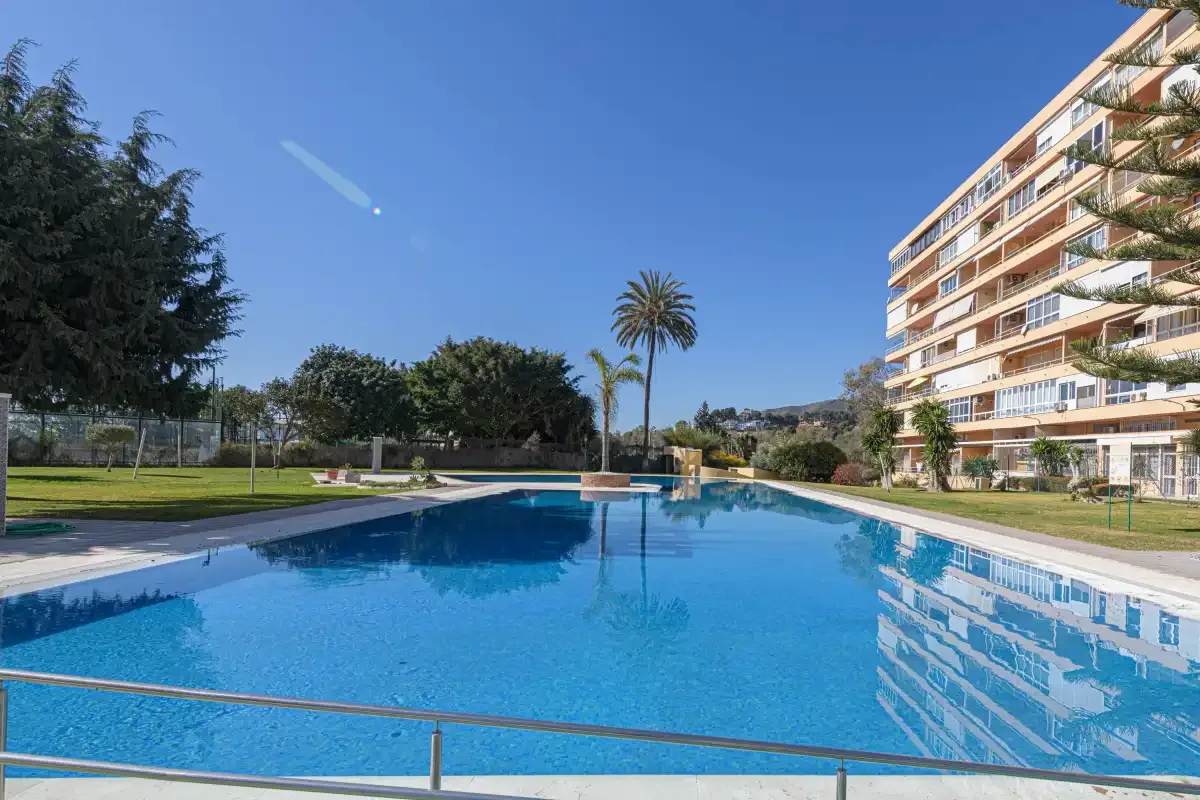 An outdoor swimming pool sits beside a multi-story residential building and landscaped grounds.