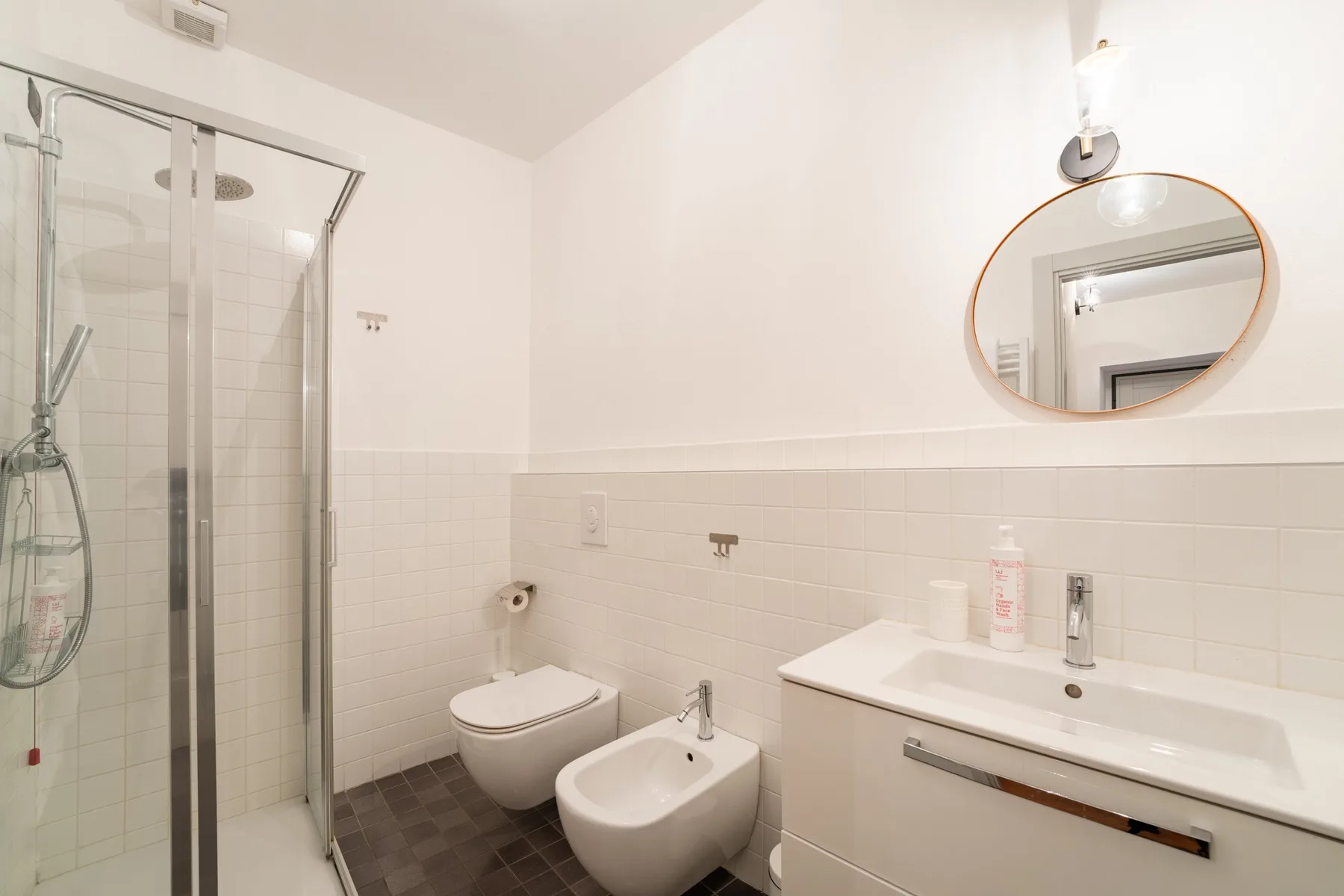 Un baño luminoso con ducha de vidrio, inodoro suspendido y lavabo.