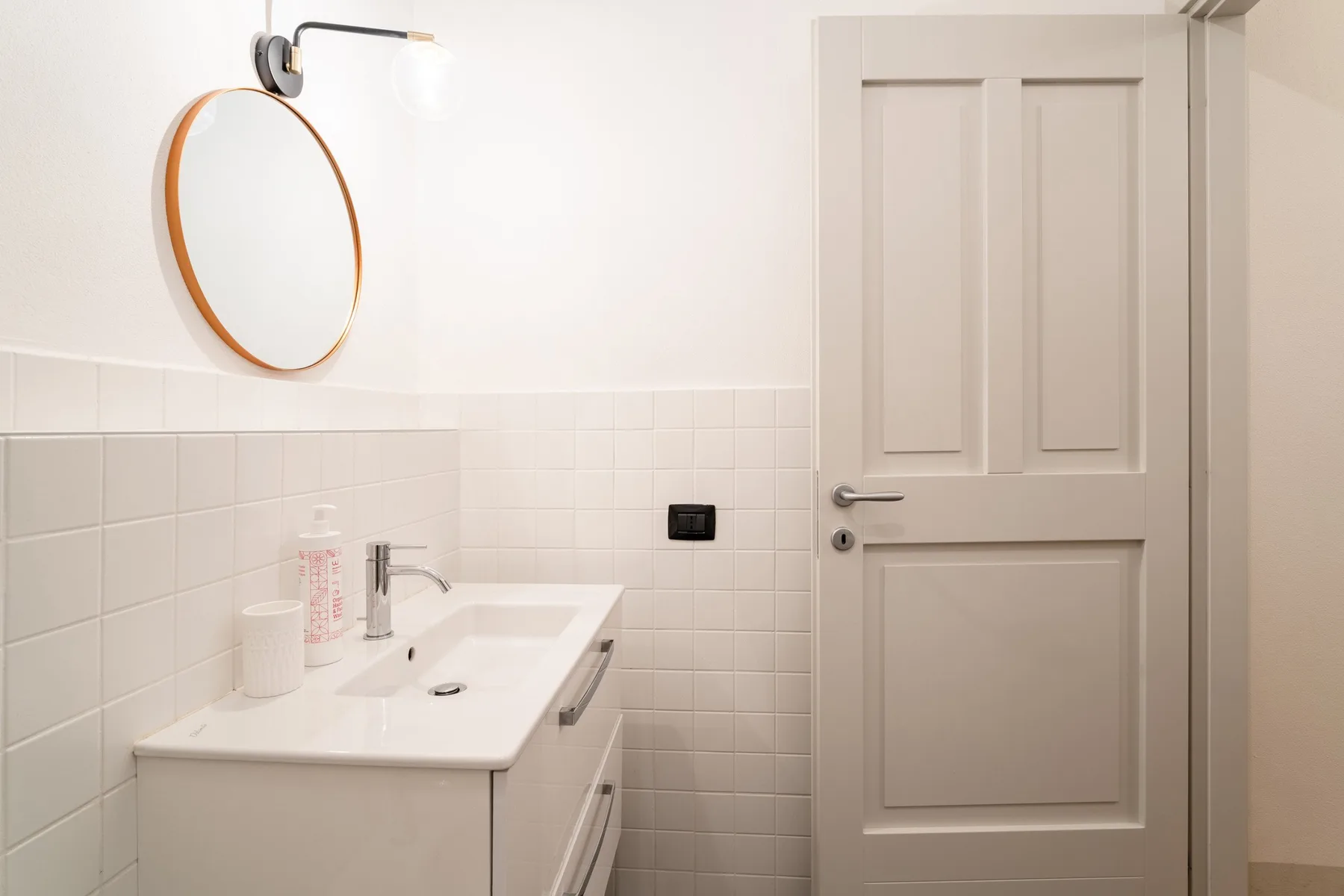 Un lavabo de baño con espejo redondo junto a una puerta cerrada.