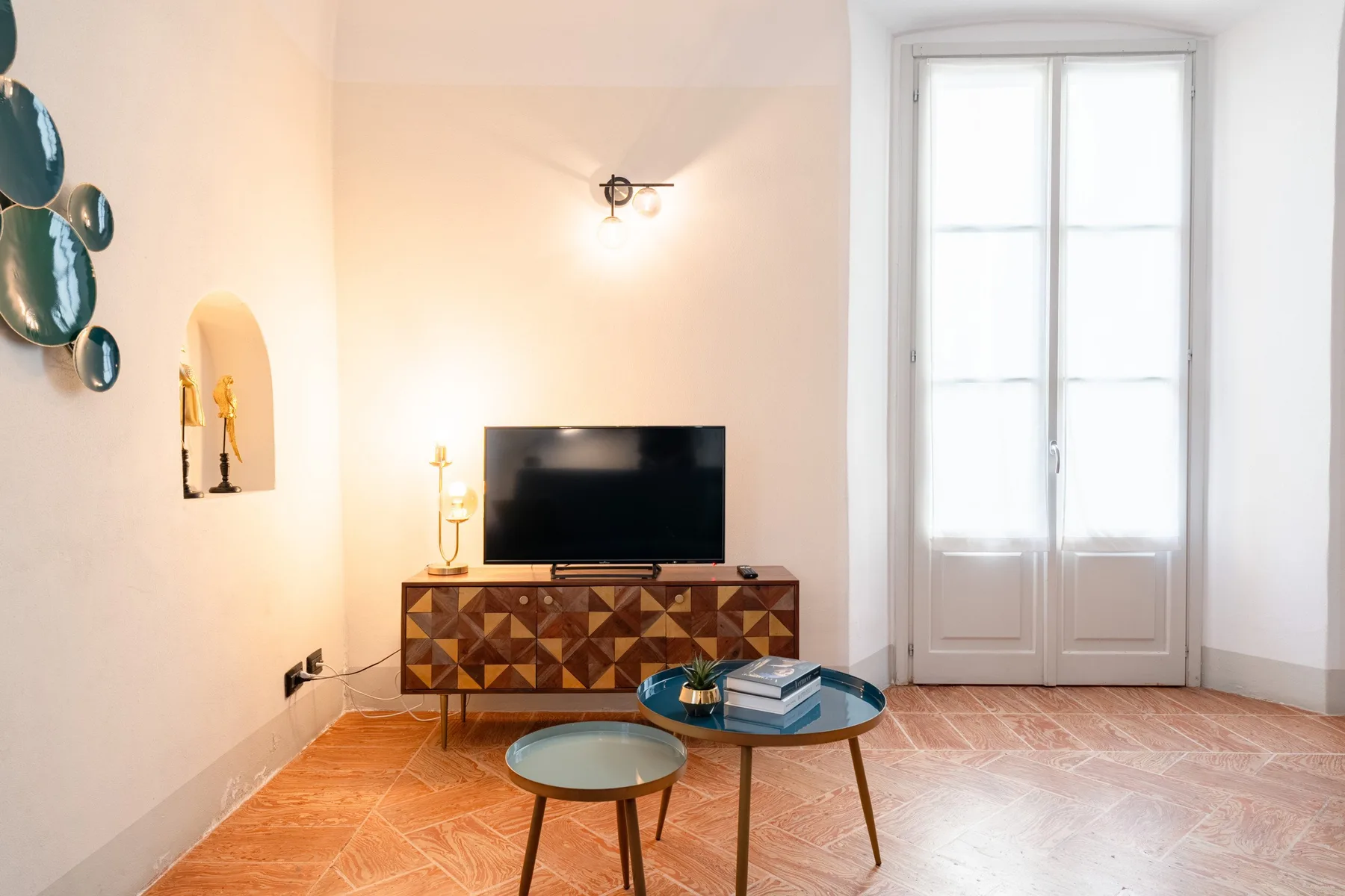 Una sala luminosa con un televisor sobre un mueble estampado y una ventana alta.