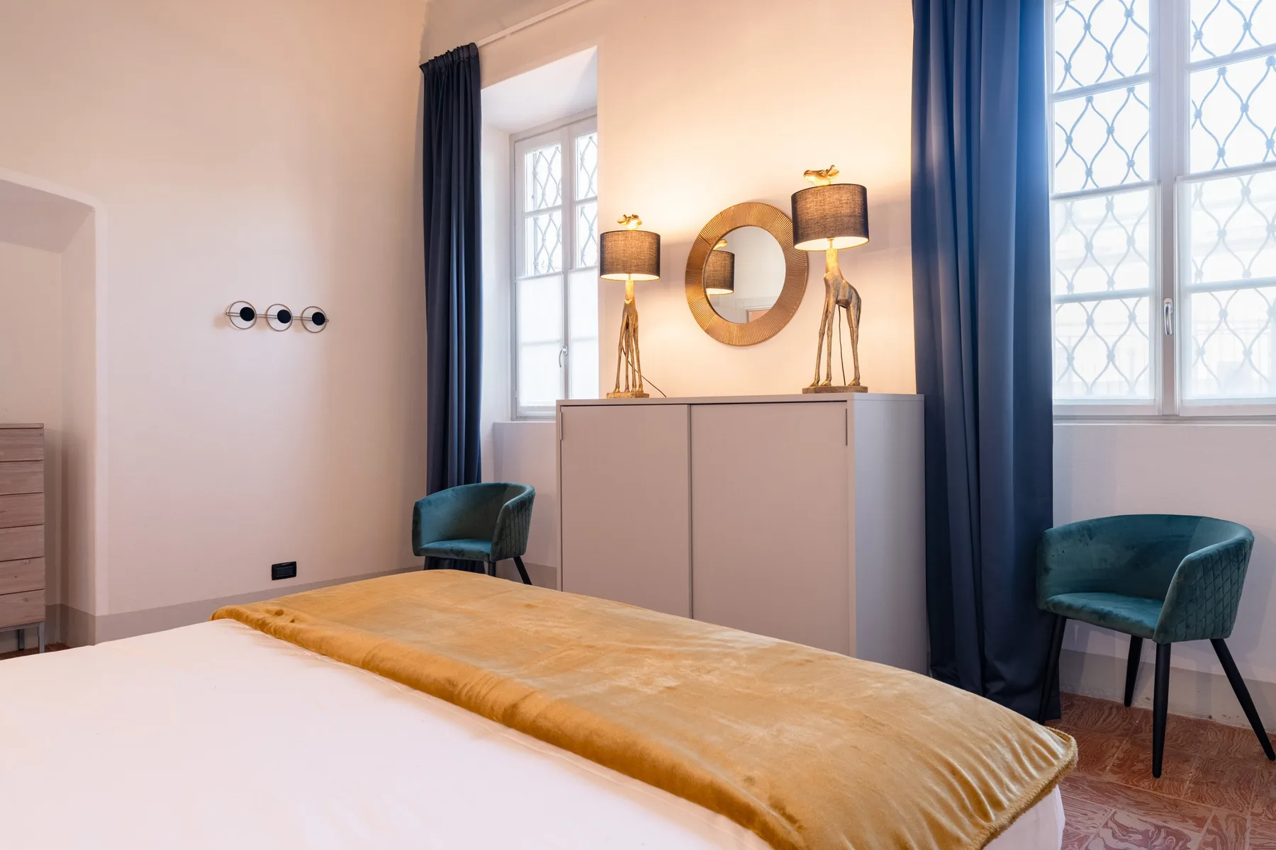Un dormitorio con una cama, un armario y ventanas altas con cortinas azules.