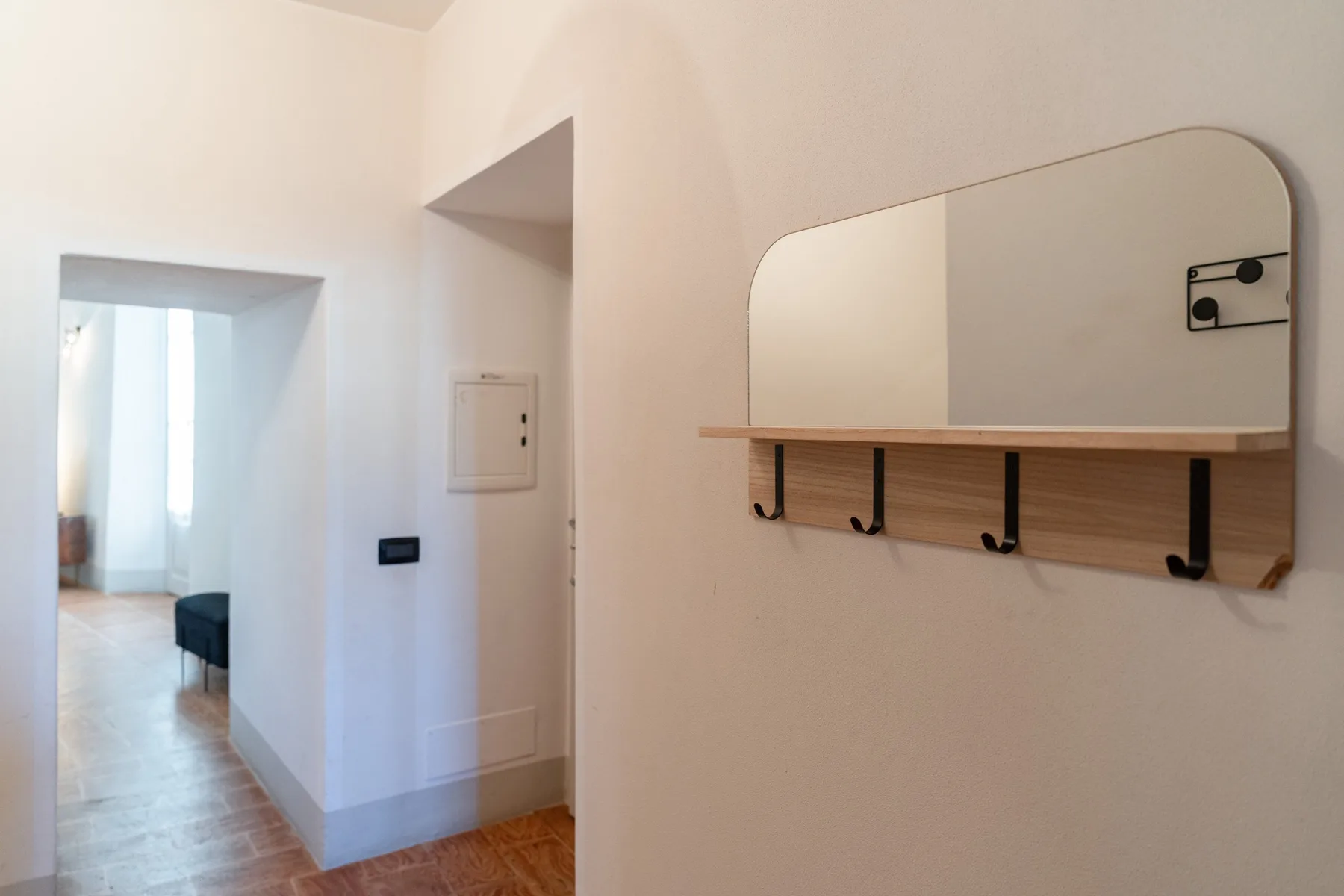 Un pasillo luminoso con un espejo de pared y una fila de ganchos debajo.