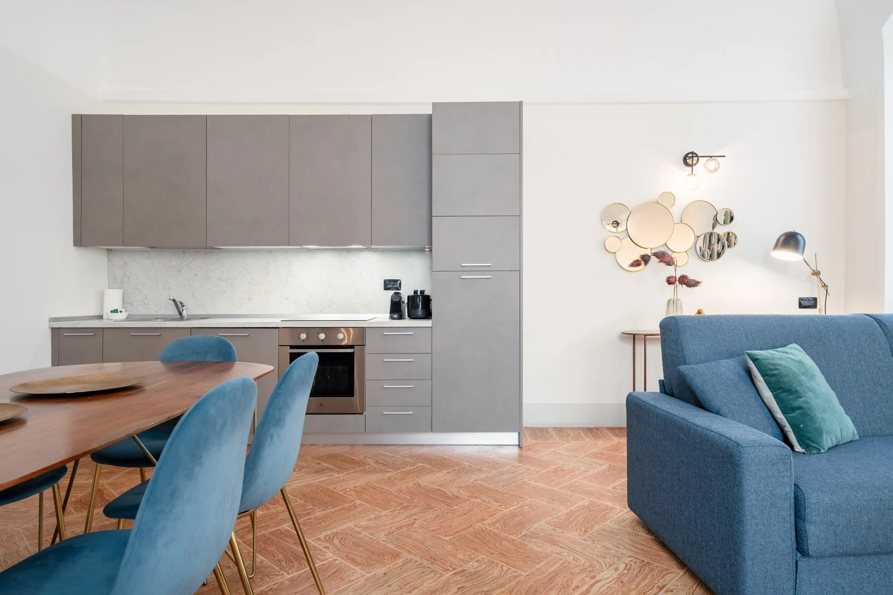 Una cocina y sala de estar de concepto abierto con asientos azules y gabinetes grises.