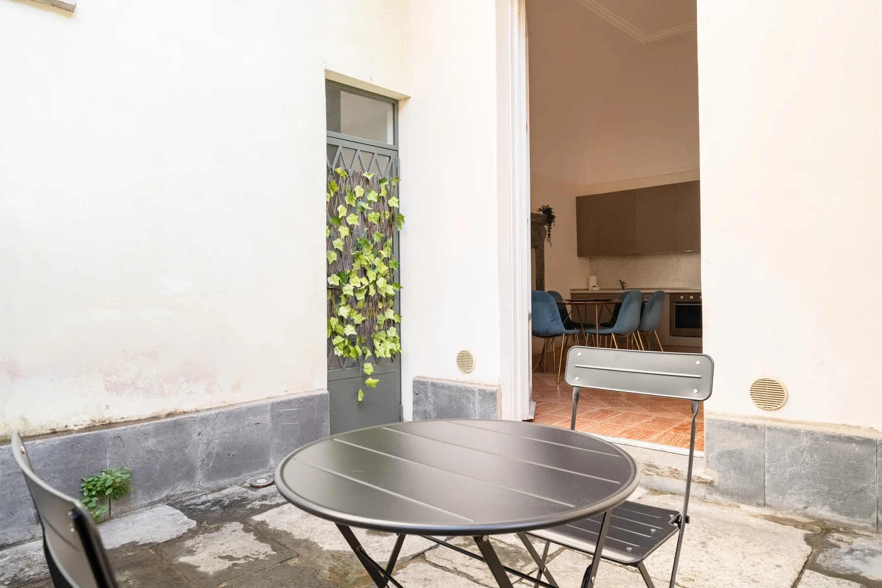 Un pequeño patio con una mesa redonda y asientos junto a una puerta abierta.