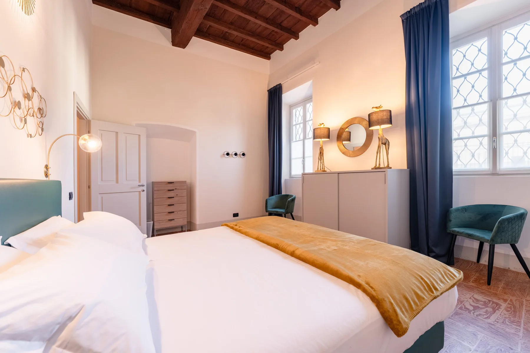 Un dormitorio con una cama, ventanas con motivos decorativos y vigas de madera a la vista.