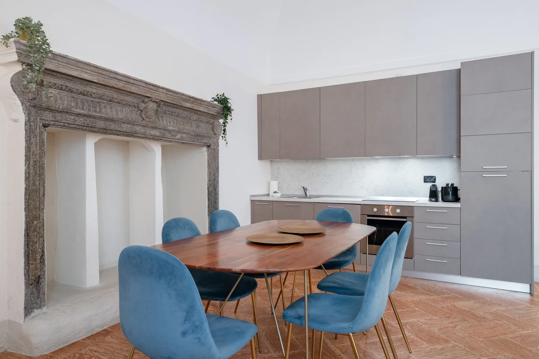Comedor con mesa de madera y asientos azules junto a una cocina moderna.